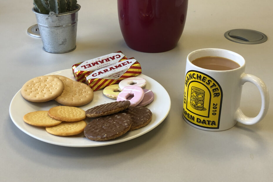 A plate of different biscuits and a mug of tea with Open Data Manchester printed on.
